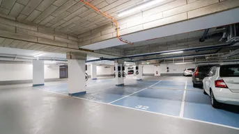 Geräumige Tiefgarage mit markierten Stellplätzen, moderner Beleuchtung und sichtbaren Installationen.
