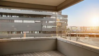 Balkon mit Holzboden und Glasbrüstung, bietet einen weiten Blick auf die Stadt und umliegende Gebäude.