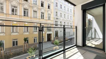 Heller Balkon mit Glasgeländer und Blick auf die gegenüberliegenden Altbauten in der Stadt.