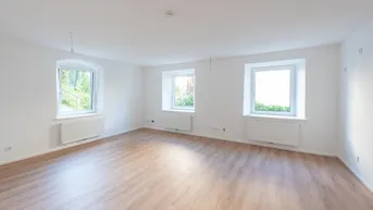 Helles, leeres Zimmer mit Laminatboden, weißen Wänden und drei Fenstern, bereit zur Gestaltung.
