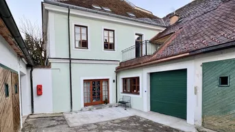 Historisches Gebäude mit hellgrüner Fassade, Holztüren und einem Garagentor im Innenhof.