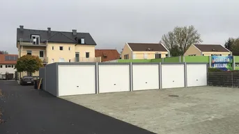 Reihe von Garagen mit weißen Toren und angrenzenden Wohngebäuden in einer städtischen Umgebung.