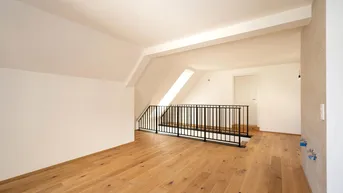 Heller Dachbodenraum mit Holzboden, Dachschräge und schwarzem Geländer, bereit für den Ausbau.