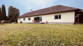 Hausrückseite mit großer Rasenfläche und einer Terrasse mit Gartenmöbeln unter bewölktem Himmel.