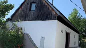 Rustikales Gebäude mit weiß getünchter Fassade und Holzdachgiebel unter blauem Himmel.
