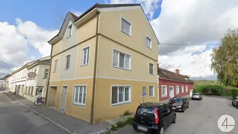 Mehrstöckiges Gebäude mit gelb-grauer Fassade und Satteldach an einer Wohnstraße gelegen.