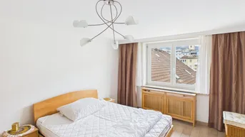 Schlafzimmer mit Holzbett, Nachttischen und Blick auf die Dächer durch das Fenster.
