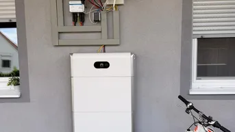 Außenwand mit installierter Photovoltaik-Anlage und Batteriespeicher neben einem Fahrrad.
