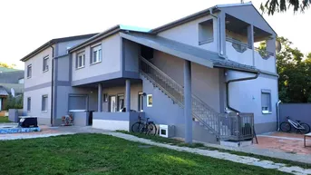 Modernes Mehrfamilienhaus mit grauer Fassade, Außentreppe und gepflegtem Vorgartenbereich.