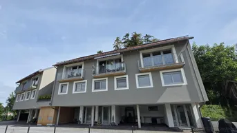 Modernes Mehrfamilienhaus mit Balkonen und grauer Fassade unter blauem Himmel.