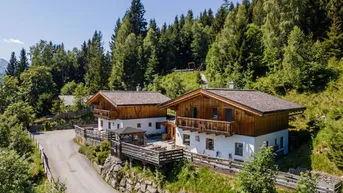 Zwei traditionelle Chalets in alpiner Umgebung mit dichtem Wald und Bergblick.