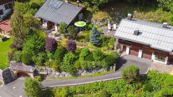 Luftaufnahme von zwei traditionellen Häusern in einer grünen, bergigen Landschaft mit üppiger Vegetation.