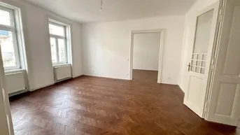 Helles Zimmer mit Fischgrätparkett, hohen Türen und Blick auf die Straße.