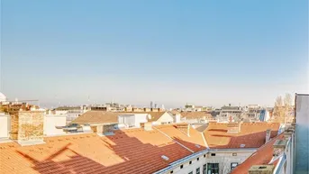 Weitläufiger Blick über die Dächer der Stadt mit roten Ziegeldächern unter blauem Himmel.