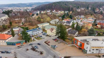 Luftaufnahme der Umgebung mit Wohngebäuden, Straßen und bewaldeten Hügeln im Hintergrund.