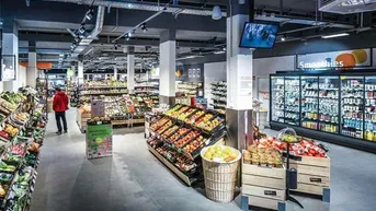 Großer, gut beleuchteter Supermarkt mit frischem Obst und Gemüse in den Auslagen und Kühlregalen.