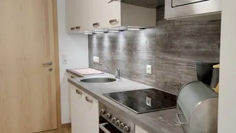 Moderne Küchenzeile mit integrierten Geräten, Spüle und Holzoptik-Arbeitsplatte.
