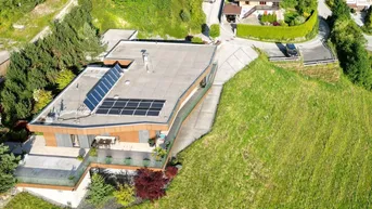 Luftaufnahme eines modernen Gebäudes mit Flachdach und Photovoltaikanlage in grüner Umgebung.