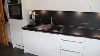 Moderne Einbauküche mit weißen Schränken, schwarzer Arbeitsplatte und integriertem Backofen.