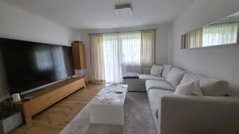 Helles Wohnzimmer mit großem Sofa, Holzboden und Zugang zum Balkon.
