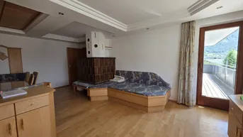 Heller Wohnbereich mit Kachelofen und Zugang zu einem großen Balkon mit Bergblick.