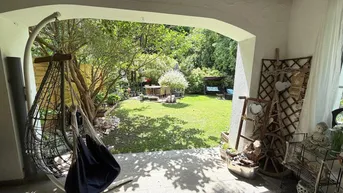Überdachte Terrasse mit Hängesessel und Blick auf den grünen Garten mit Sitzbereich.