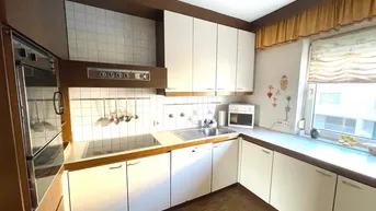 Küche mit weißen Einbauschränken, Holztheke, integrierten Geräten und Fliesenrückwand.