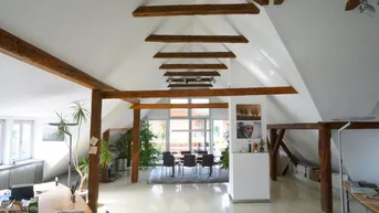 Geräumiges Dachgeschossbüro mit sichtbaren Holzbalken, hohen Decken und viel natürlichem Licht.