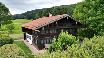 Traditionelles Holzhaus mit rotem Ziegeldach, grüner Umgebung und weitem Blick auf die Landschaft.