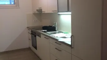 Helle Einbauküche mit weißen Schränken, Fliesenboden und Fenster für Tageslicht.
