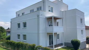 Modernes Mehrfamilienhaus mit weißer Fassade und Balkonen in grüner Umgebung.