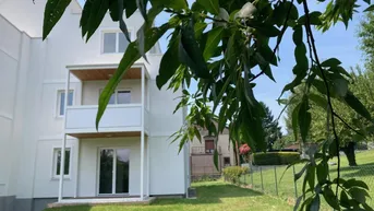 Weißes Mehrfamilienhaus mit Balkonen und direktem Zugang zum grünen Gartenbereich.