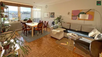 Helles Wohn- und Esszimmer mit Parkettboden, großen Fenstern und einem weiten Blick über die Stadt.