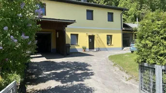 Gelbes Wohnhaus mit Garage, langer Auffahrt und umgebender grüner Natur.