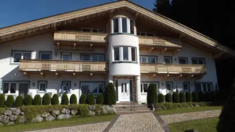 Traditionelles Gebäude im alpinen Stil mit Holzbalkonen und gepflegtem Vorgarten.