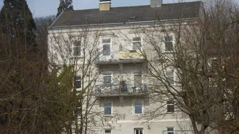 Mehrfamilienhaus mit grauer Fassade und mehreren Balkonen, umgeben von Bäumen.