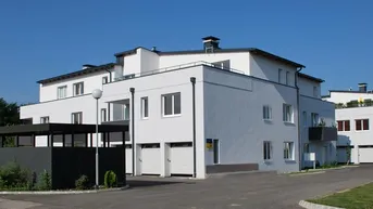 Modernes Mehrfamilienhaus mit weißer Fassade, Flachdach und integrierten Garagen in gepflegter Umgebung.
