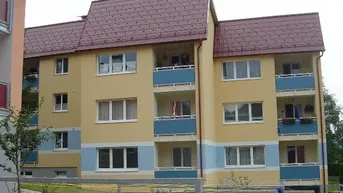 Mehrstöckiges Wohngebäude mit gelber Fassade, blauen Balkonen und einem markanten Mansarddach.