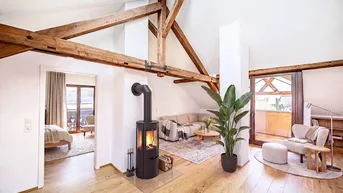 Helles Wohnzimmer mit Holzbalken, Kaminofen und Zugang zu einem Schlafzimmer.