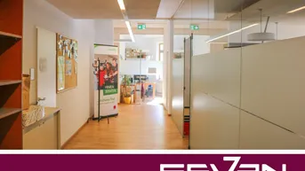 Heller Bürogang mit Glaswänden und Holzfußboden, der zu weiteren Arbeitsbereichen führt.