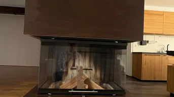 Moderner freistehender Kamin mit Glasfronten, umgeben von Holzboden und offener Raumgestaltung.