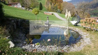 Natürlicher Gartenteich mit Schaukelstuhl in einer hügeligen Landschaft mit Bäumen und Herbstfarben.