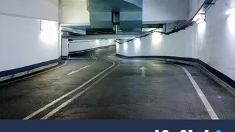 Zufahrtsrampe einer Tiefgarage mit hellen Wänden, Asphaltboden und sichtbaren Lüftungsanlagen.