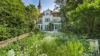 Historische Villa mit weitläufigem Garten und Blick auf die Kirchturmspitze.