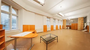 Geräumiger, heller Raum mit hohen Decken, Holzvertäfelung und großen Fenstern zur Straße.