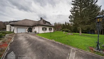 Einfamilienhaus mit großer Auffahrt und gepflegtem Vorgarten unter bewölktem Himmel.