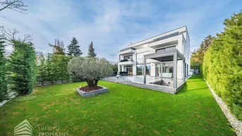 Moderne Villa mit großem Garten, Pool und gepflegter Rasenfläche unter blauem Himmel.