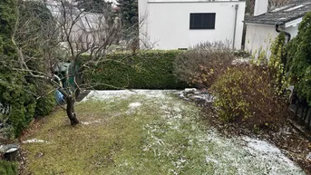 Gartenbereich mit Rasenfläche, Bäumen und Hecke, leicht mit Schnee bedeckt, im Hintergrund ein modernes Wohnhaus.