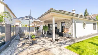Überdachte Terrasse mit Essbereich, Liegestühlen und einem dekorativen Wasserbecken im Garten.