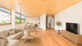 Helles, offenes Wohn- und Esszimmer mit integrierter Küche, Holzboden und großen Fenstern mit Blick ins Grüne.